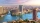 Aerial view of downtown Cairo with the Nile River, high-rise buildings, boats on the water, and a hazy skyline under a pink and blue sky at sunset.